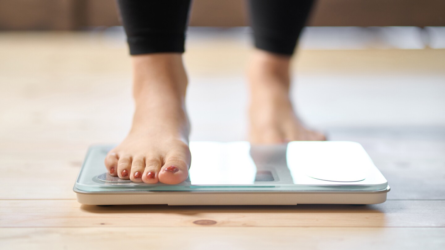 Feet of a person with red-painted toenails as the person steps onto a weight scale.