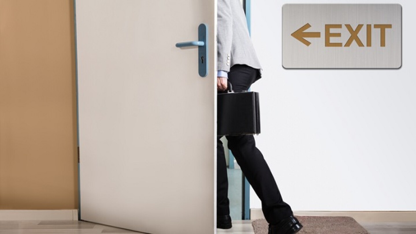 Businessperson Walking Out With Exit Sign On Wall