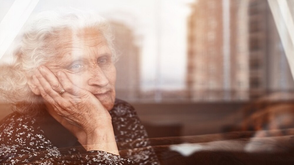 Elderly woman sitting alone and looking sadly outside the window