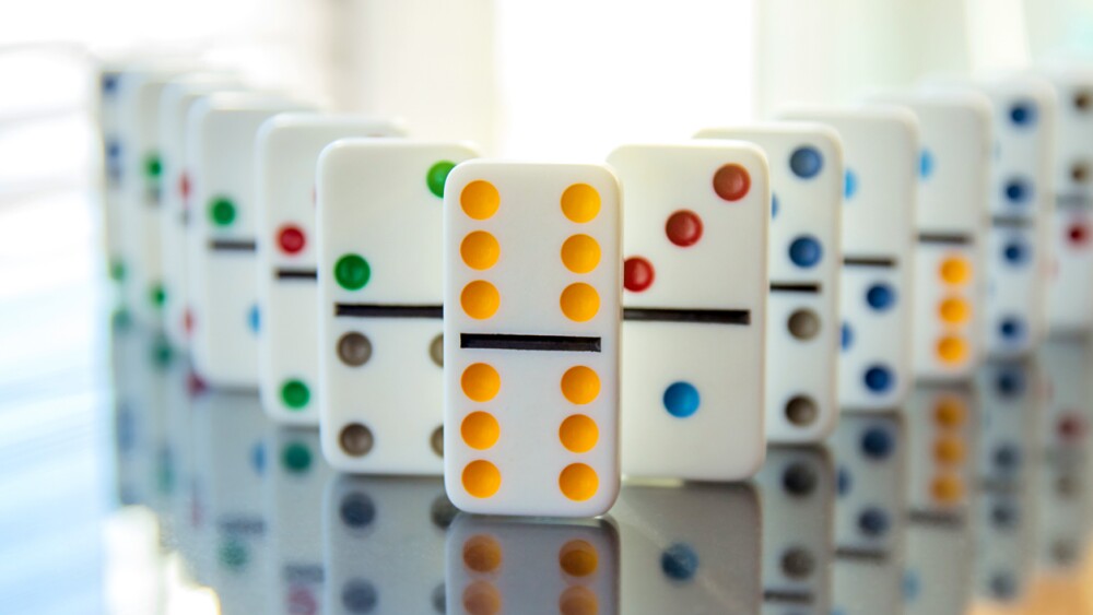 white dominoes stand in row on mirror surface with double six leading the way.