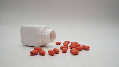 Open white medication bottle tipped over with red capsules scattered on a plain background, highlighting modern healthcare and medication management.