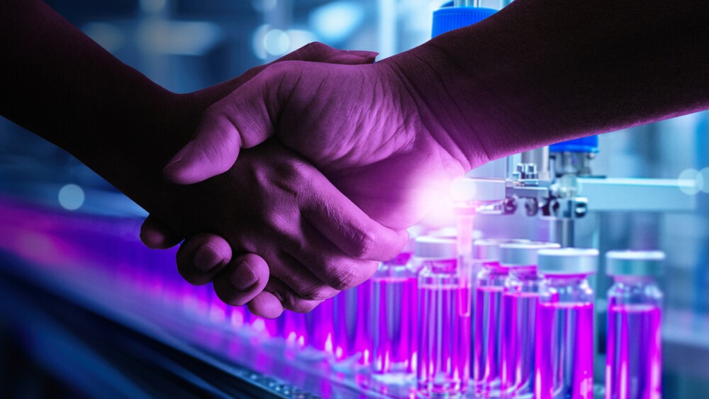 Two individuals shake hands in front of advanced laboratory equipment, symbolizing a partnership or agreement in the pharmaceutical industry.