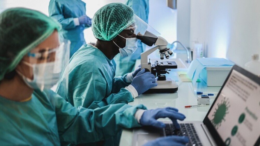 Multiracial medical scientists in hazmat suit working with microscope and laptop computer inside modern laboratory hospital - Focus african man face