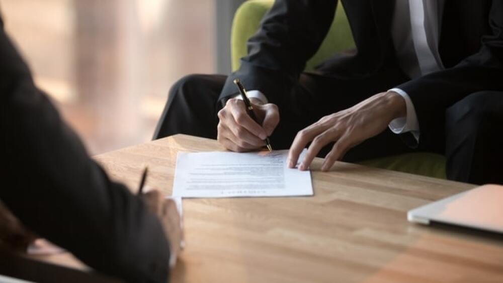 Pictured: Two people signing contracts/Courtesy of