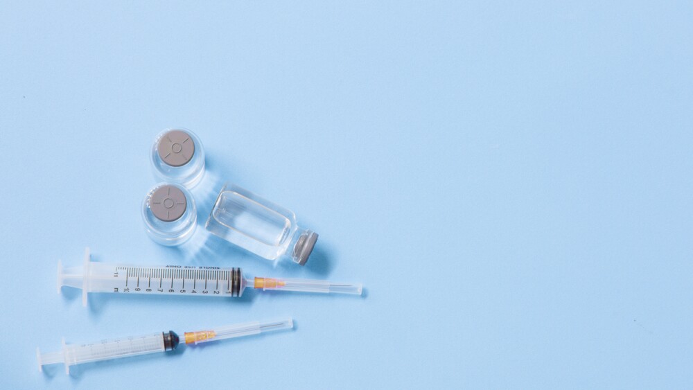 Close-Up Of Syringe With Bottles Against Blue Background